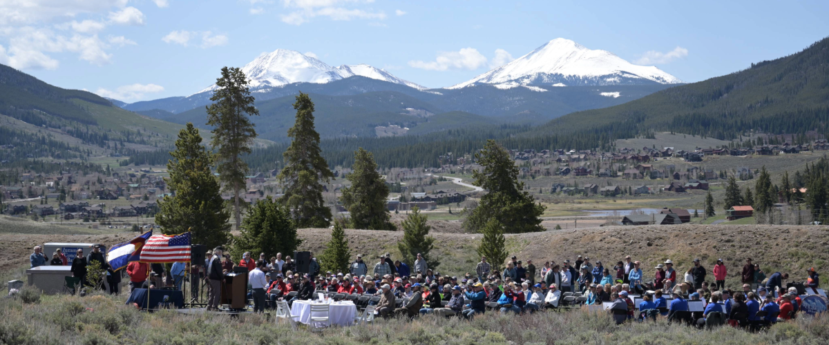 A diverse crowd of people stands in front of a majestic mountain range, enjoying the scenic view together.