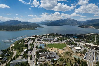 Aerial view showcasing a serene lake surrounded by majestic mountains under a clear blue sky.