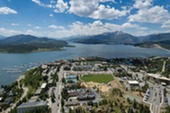 Aerial view showcasing a serene lake surrounded by majestic mountains under a clear blue sky.