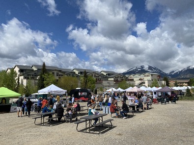 A bustling farmers market in the mountains, with people browsing fresh produce and local goods amidst scenic views.