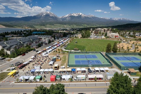 Aerial view of a tennis court surrounded by mountains, showcasing the court's vibrant colors against a natural backdrop.