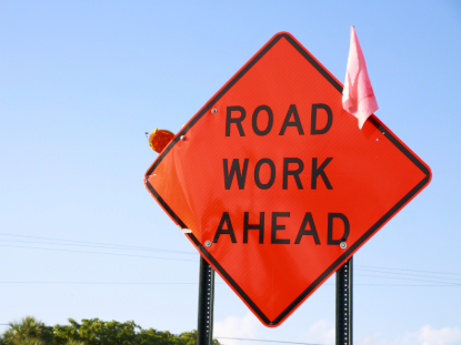 A cautionary road work ahead sign, featuring bold black lettering on a yellow background, warning drivers of upcoming work.