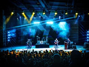 A band performs on stage, illuminated by vibrant lights, creating an energetic atmosphere for the audience.
