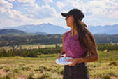 A woman holds a frisbee with the mountains in the background