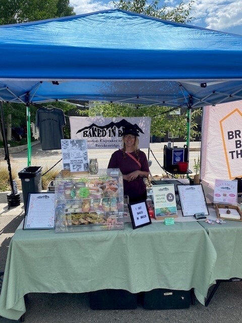 A woman stands behind a table filled with various dishes, smiling as she prepares to serve food to guests