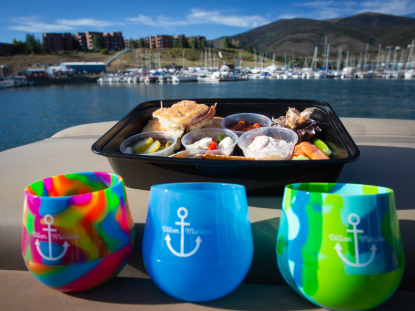 A tray of gourmet food and wine glasses elegantly arranged on a boat deck, with water in the background.