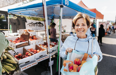 A woman holds a bag filled with fresh fruits and vegetables, showcasing a healthy selection of produce