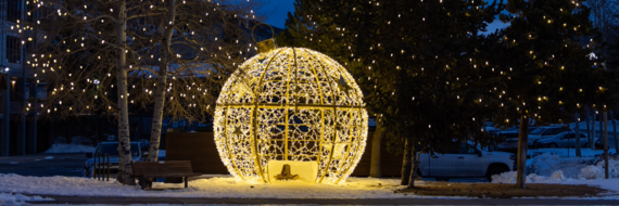 a giant ornament illuminated against a snowy background with twinkling lights in the trees