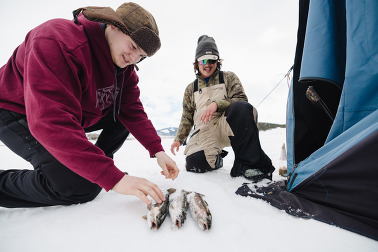 Two people look down on three fish after an afternoon of fishing on a frozen lake