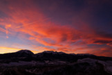 A vibrant sunset paints the sky in hues of orange and pink over a silhouette of majestic mountains