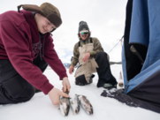 a man holds a fish while another fisherman looks on 