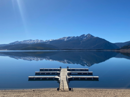 A boat dock sits reflecting on the water with mountains in the distance