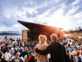 A couple sits together on the steps of a concert stage, enjoying the performance and the lively atmosphere around them.