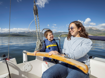 A child and a woman sailing a boat on a body of water with a mountain scenery in the distance 