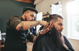 Barber cutting a client's hair in a chair and cape with clippers