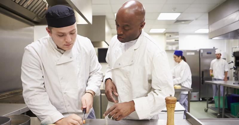 Culinary apprentice cutting vegetables with mentor chef