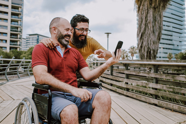 Man in wheelchair looking at phone with another man.