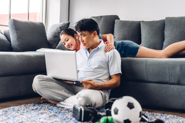 Man sitting on floor using a laptop with women behind him on a couch.