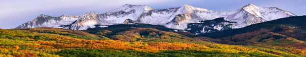 A mountain landscape with snow-capped peaks and forests showing autumn colors