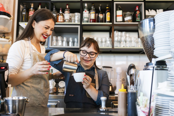 Female barista with development disabilities pouring a latte with another barista supervising