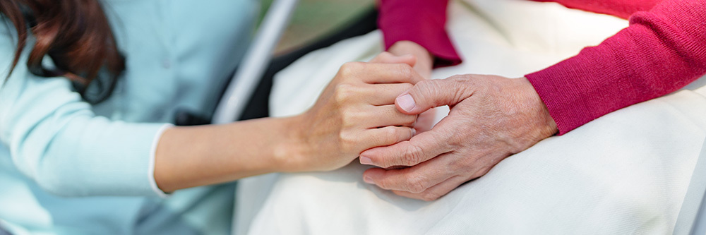 A woman reaches out to her elderly mother in a comforting gesture