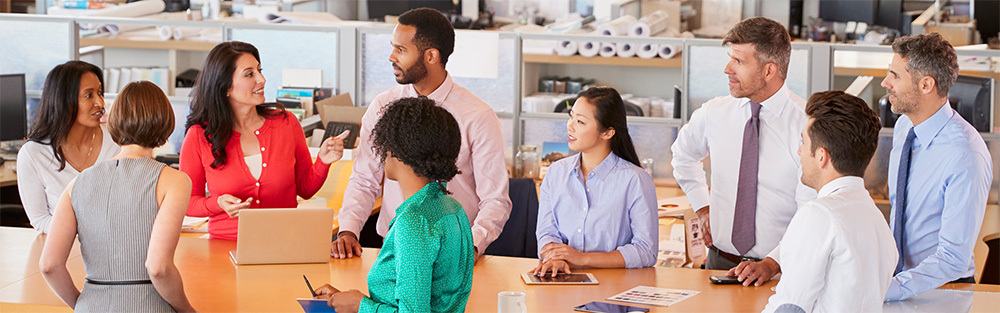 A group of professionals in an office setting stand around a conference table
