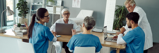 A group of medical professionals discuss cases around a conference table.