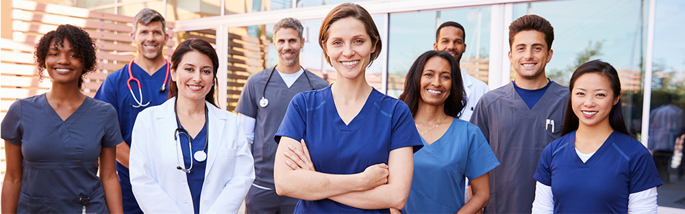 A group of smiling medical professionals stand outside a hospital.