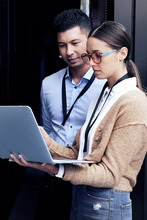 Two workers look at a laptop in a server room environment.