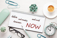 XX notebook with NOW written next to a clock on a desk