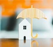 Model of umbrella with house on wooden table concept of the system of insurance savings and Housing insurance