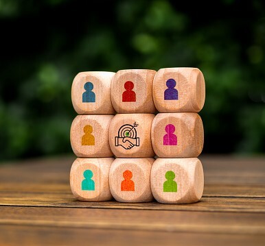 Target with handshake deal icon surrounded with multicolor businessman symbol on white cube blocks stacked as one