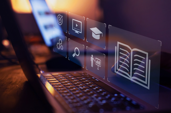 Laptop keyboard with digital icons floating above the screen, including book, graduation cap, gears, and video symbols.