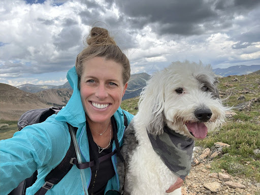 Beth and her dog pose for a selfie while hiking in the mountains. 
