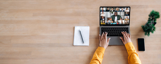 Desk with an open laptop showing a virtual meeting and hands on the keyboard