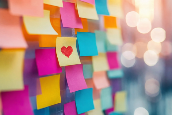 Colorful sticky notes on a glass wall with a red heart drawn on the center note, symbolizing appreciation and collaboration.