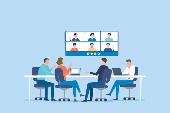 Four colleagues sitting at a table watching a monitor with a zoom meeting in progress
