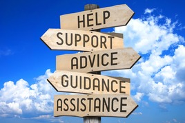Wooden directional signs displaying the words Help, Support, Advice, Guidance, and Assistance against a blue sky with clouds