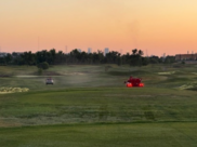 Two trucks are driving on a golf course fairway, spraying fertilizer.
