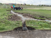A picture of two men installing a catch basin, adding drainage pipes and rocks, and laying sod grass
