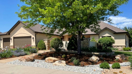 A waterwise landscaped yard with rocks, mulch, bushes and a tree.
