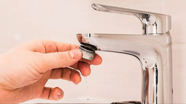 A person unscrews an aerator from the end of a bathroom faucet.