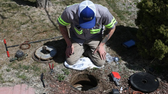 A Utility Metering Solutions staff member kneels to replace a customer's water meter.