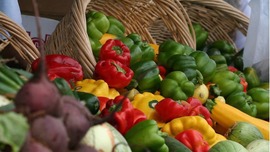 Piles of red, yellow and green peppers spill out of a wicker basket at the farmers' market