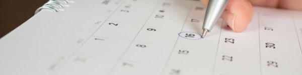 Closeup of someone holding a pen and circling a date on a calendar