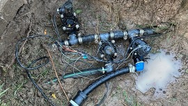 Dug-up irrigation lines lay in a puddle of water from a leak