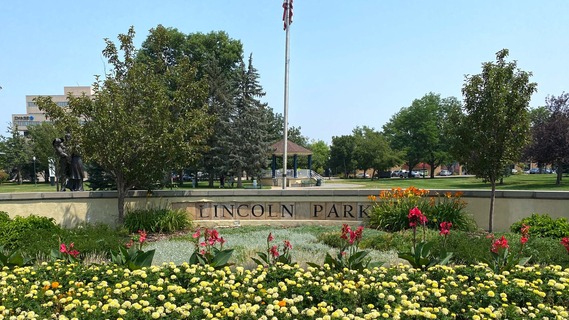 Lincoln Park entry with American flag and gazebo in background. Flowers in the foreground. 