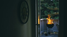 A large flame rises from a charcoal grill on a patio beneath the trees