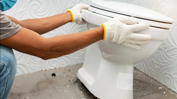 Person dislodges an old toilet from the floor.