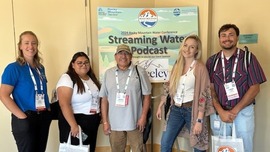 Group of people stand in front of a promotional podcast sign.